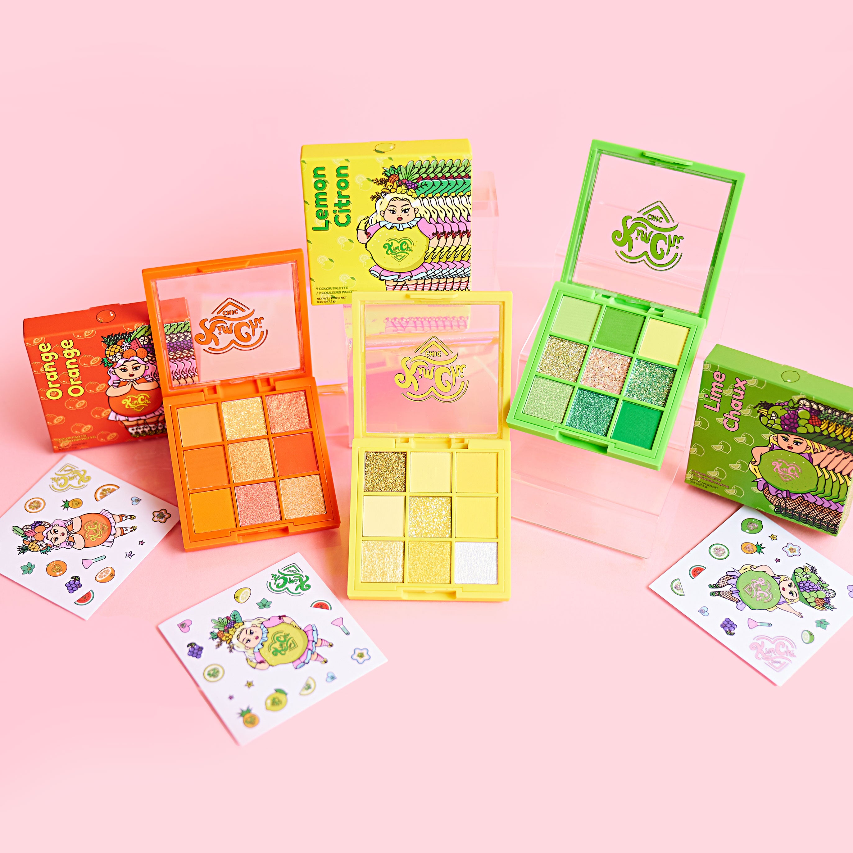 Colorful makeup palettes with fruit-themed packaging on a pink background.