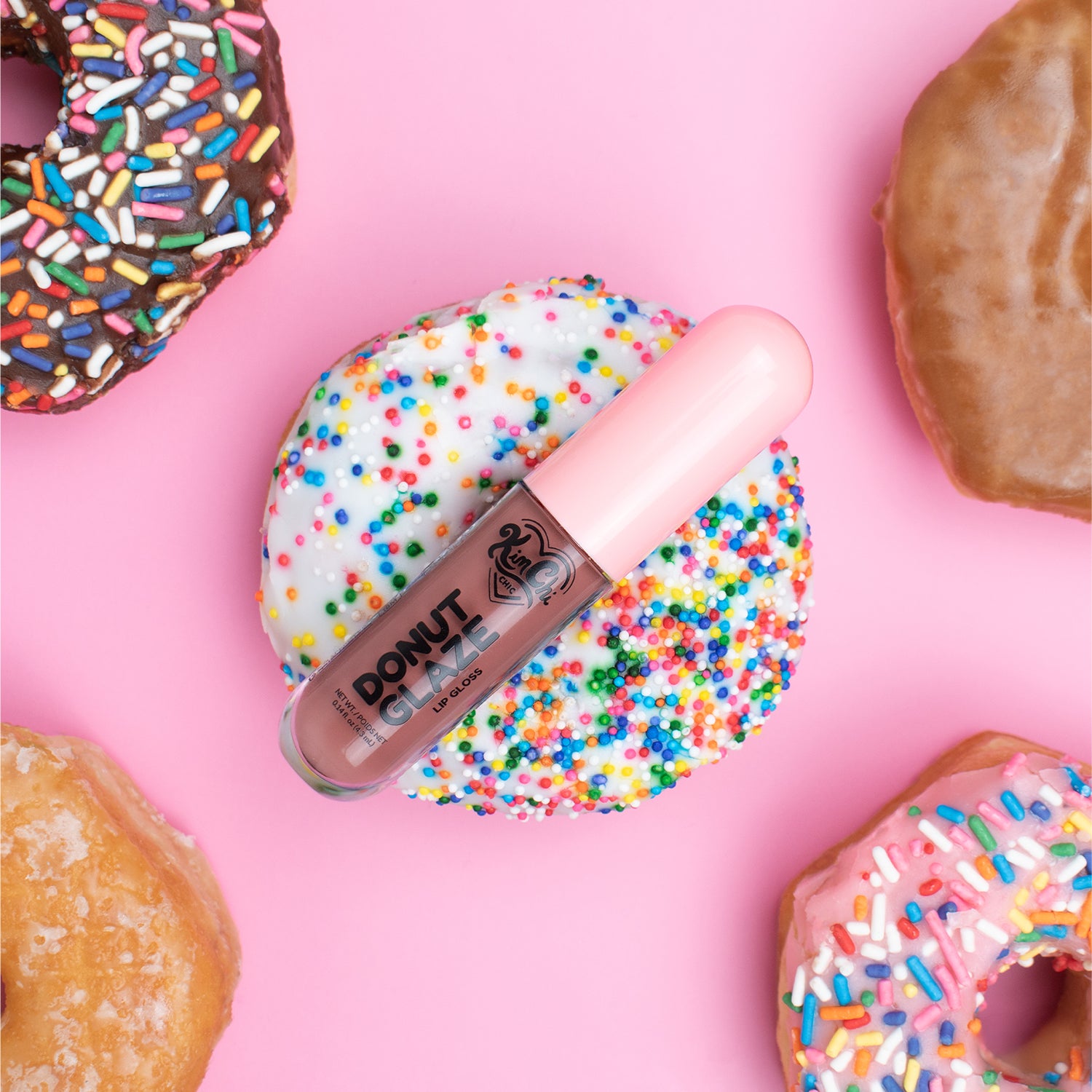 A donut topped with colorful sprinkles alongside a lip product on a pink background.
