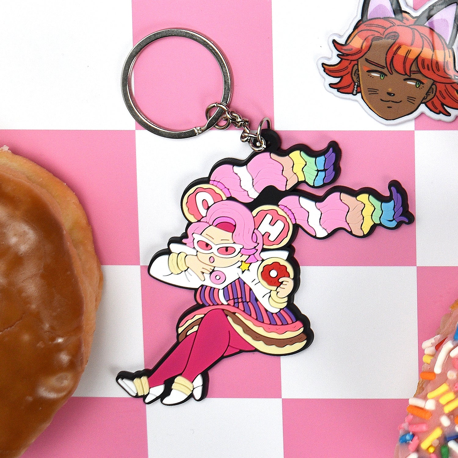 Cartoon character keychain sitting with a donut, surrounded by colorful dessert-themed elements.