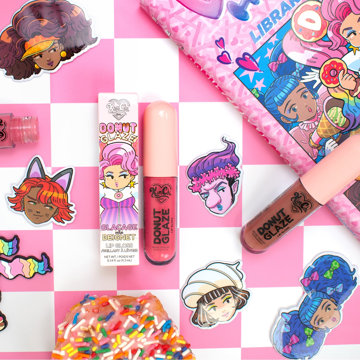 Flat lay of colorful lip products, stickers, and a donut-themed decoration on a pink checkered background.