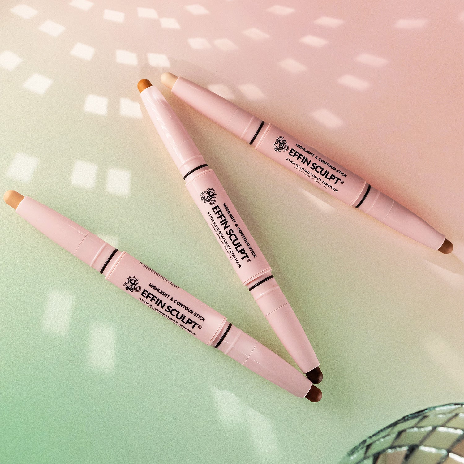 Three dual-ended cosmetic highlighting crayons on a gradient surface.