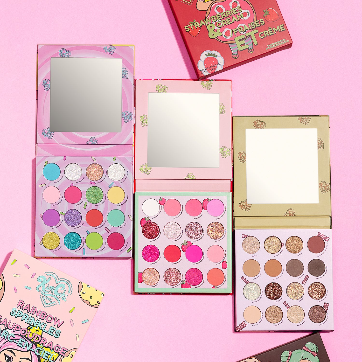 Flat lay of colorful eyeshadow palettes on a pink background.