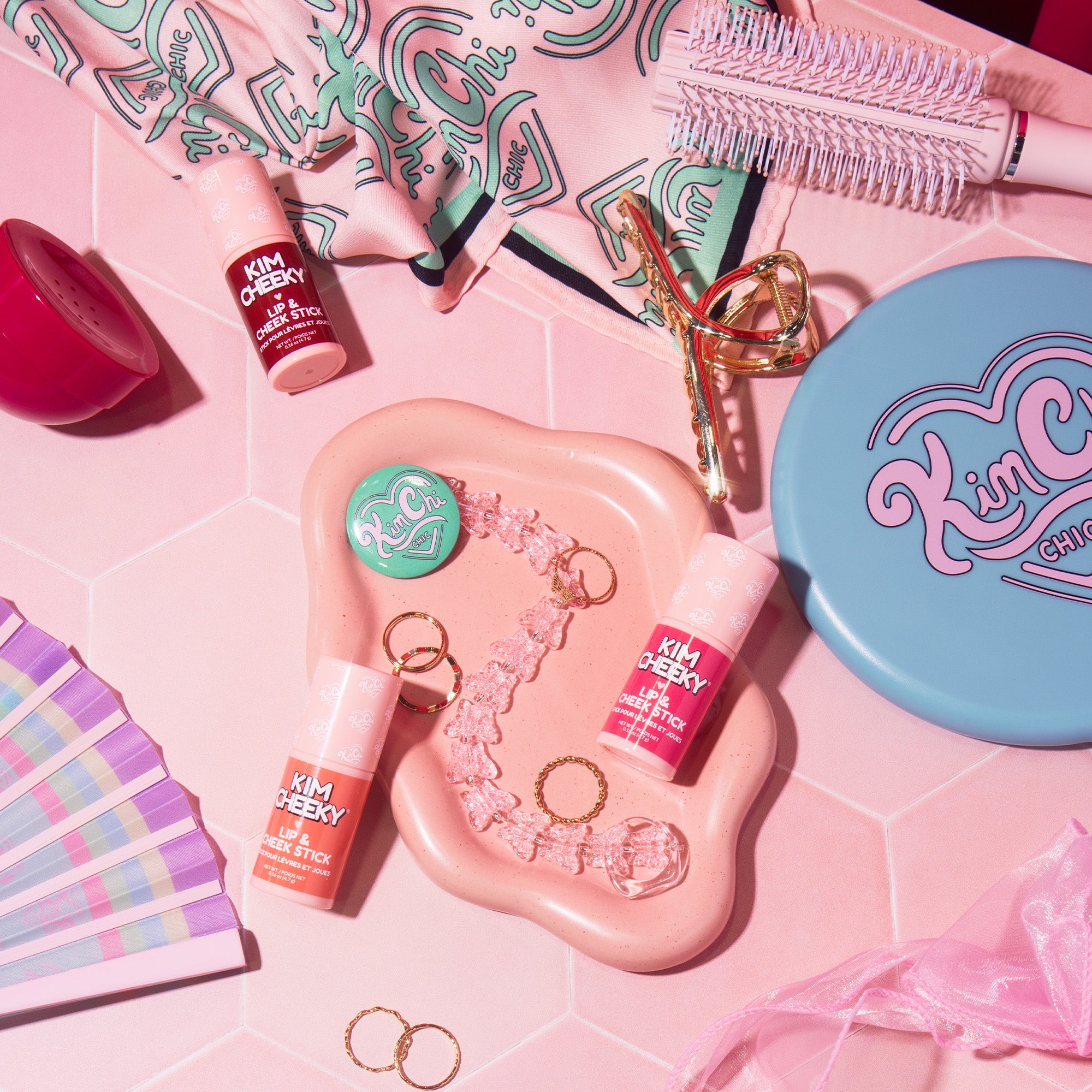 Array of beauty products and accessories arranged on a pink surface.
