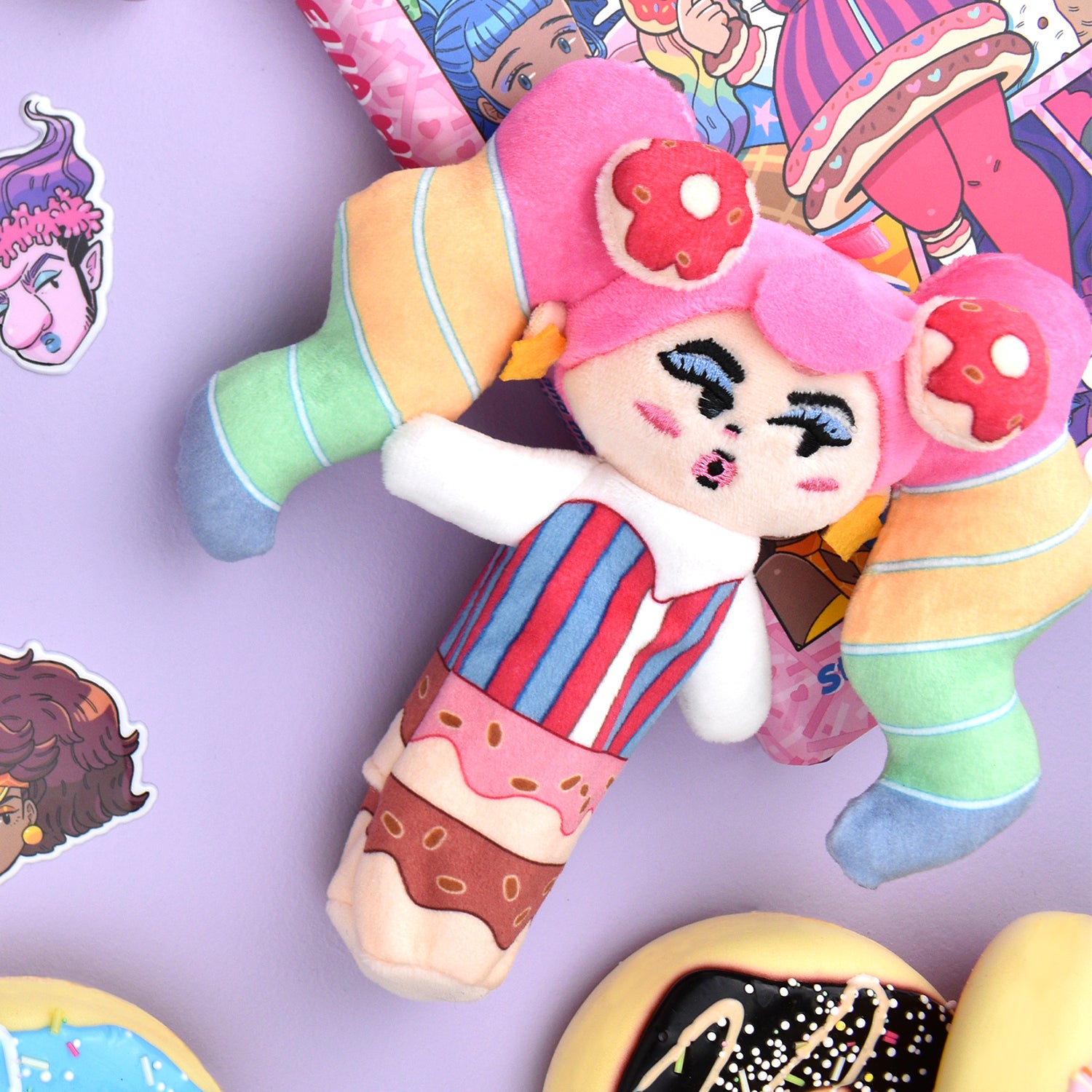 Colorful plush toy with pink hair and candy-themed outfit, surrounded by stickers and sweets.