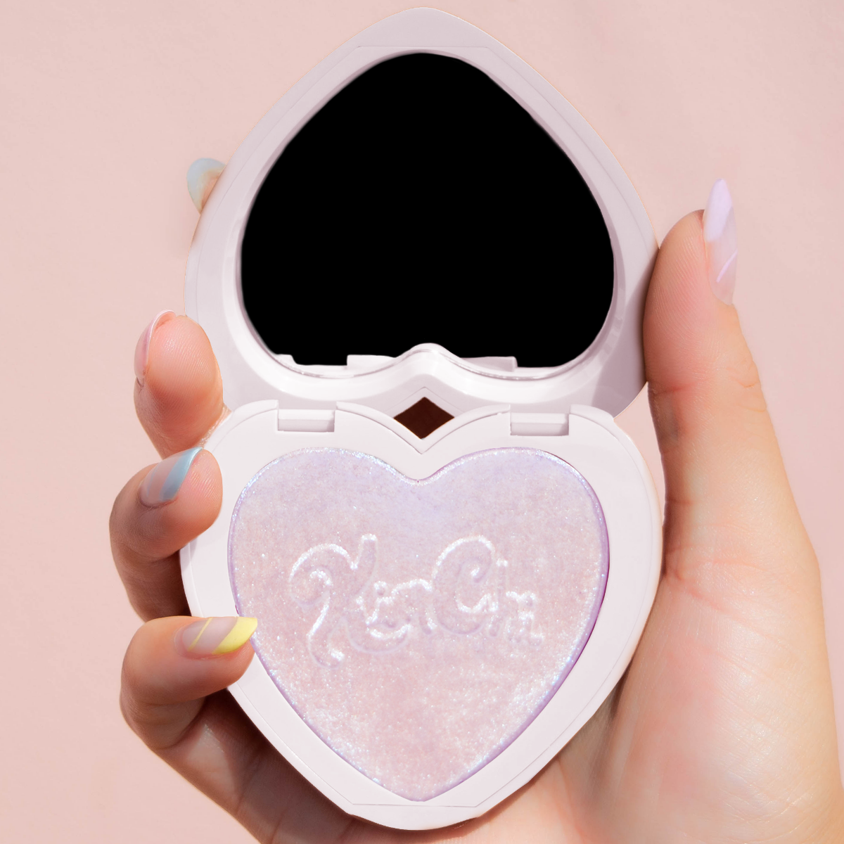 Hand holding a heart-shaped makeup compact with a shimmering powder inside.