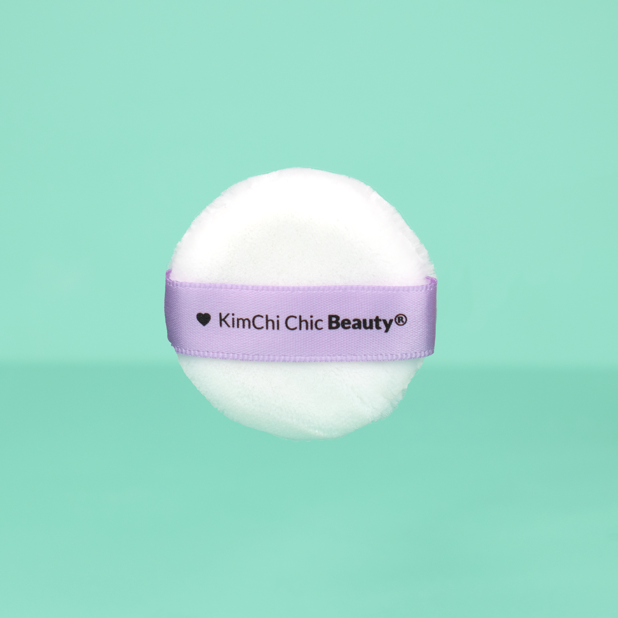 Soft white powder puff with purple KimChi Chic Beauty® logo for applying makeup smoothly.