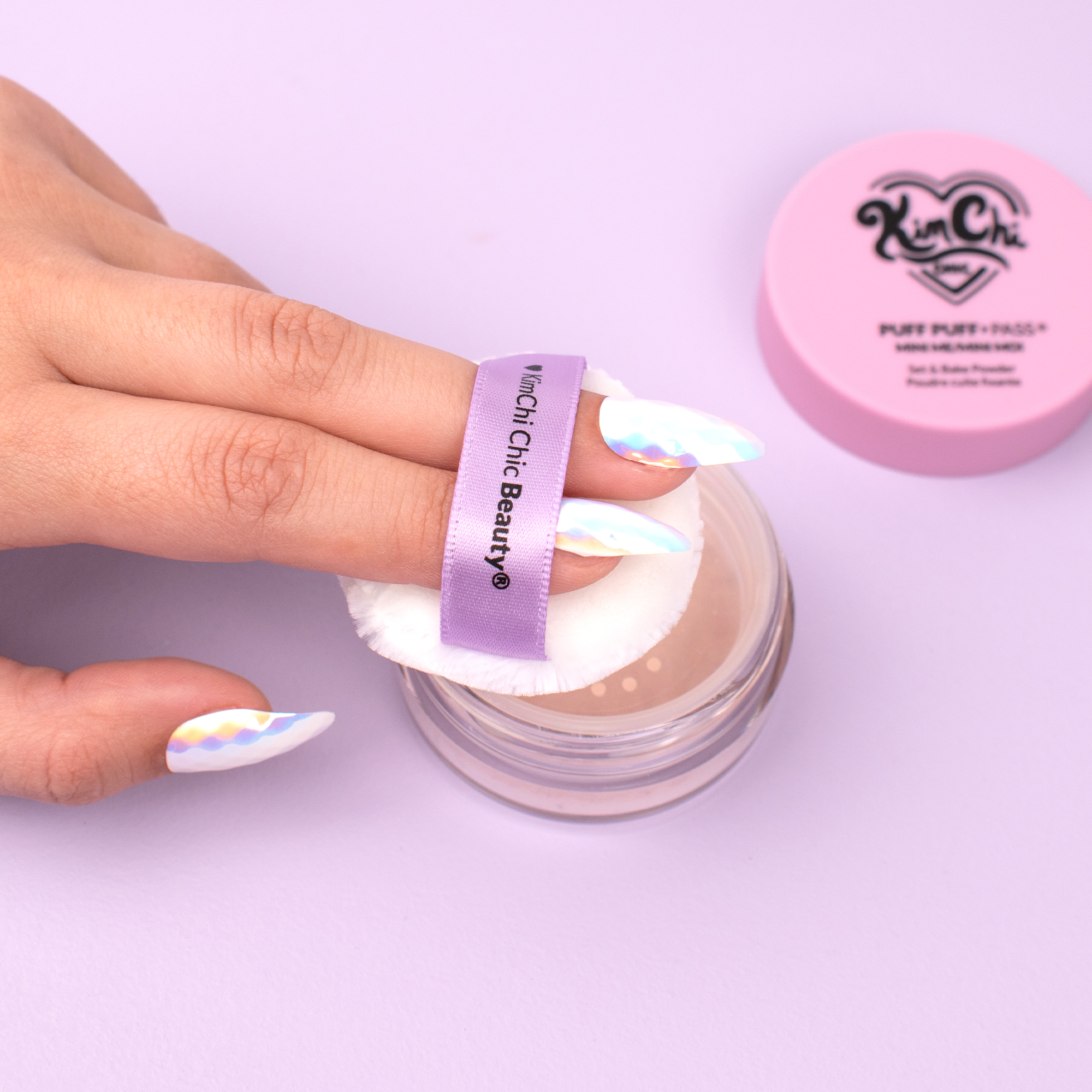 Kim Chi Chic Beauty Puff Puff Pass setting powder with applicator on hand, featuring stylish nail art.