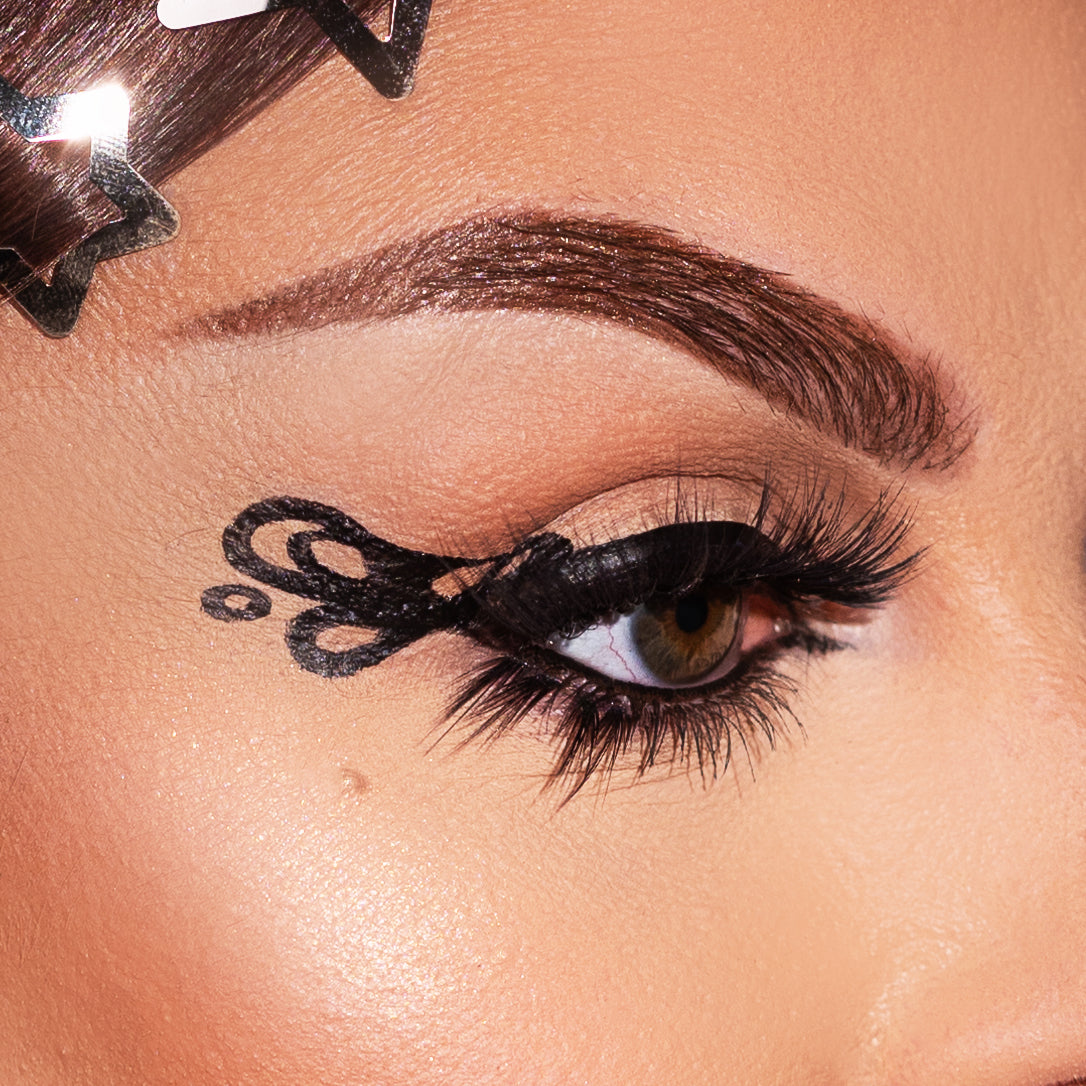 Close-up of an eye with artistic black eyeliner designs and long eyelashes.