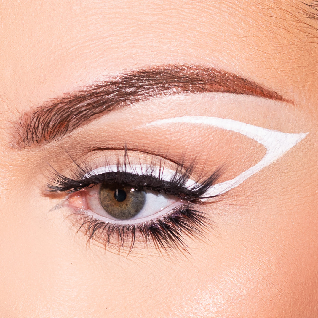 Close-up of a woman's eye with unique white eyeliner design and long eyelashes.