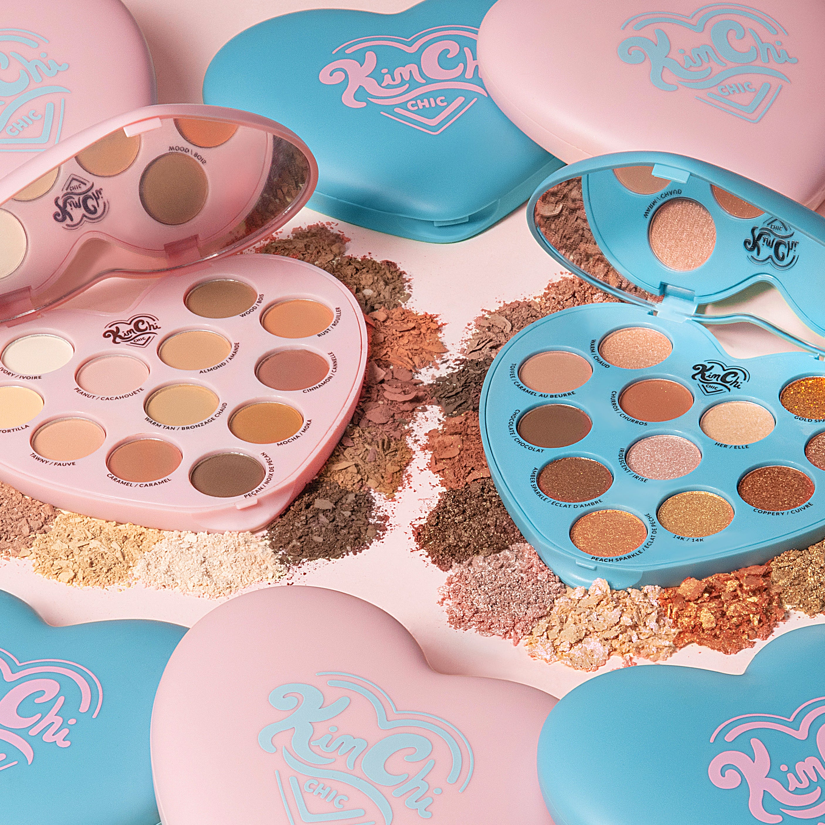 Two heart-shaped eyeshadow palettes in pink and blue, surrounded by loose pigments and shadows.