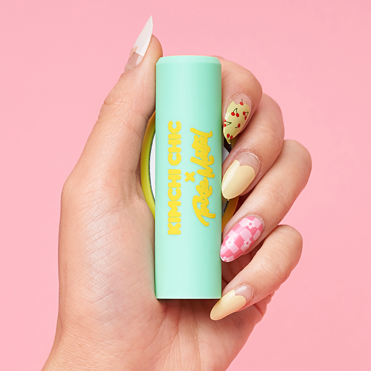 Hand holding a Kimchi Chic x Trixie Mattel lipstick tube against a pink background