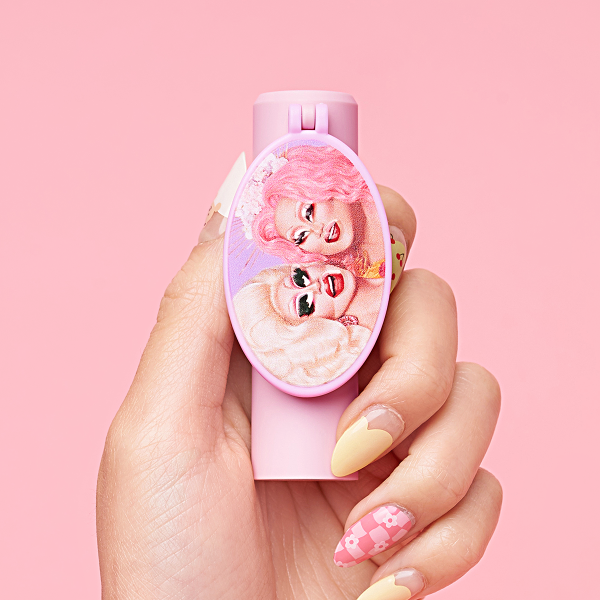 Hand holding a pink lipstick with an illustrated design of two faces on the cap