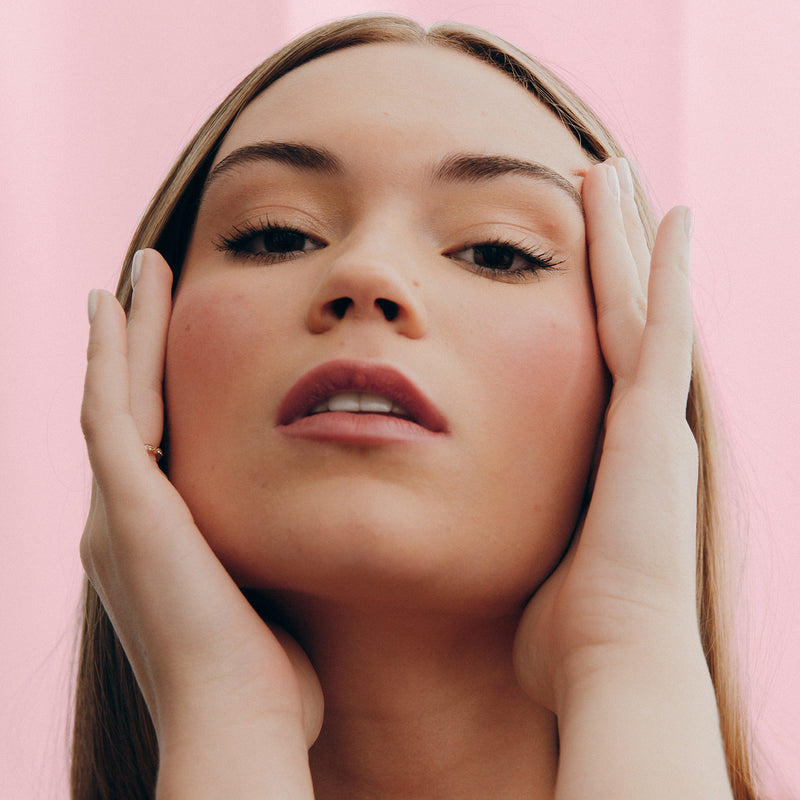 Woman posing with hands on face against pink background