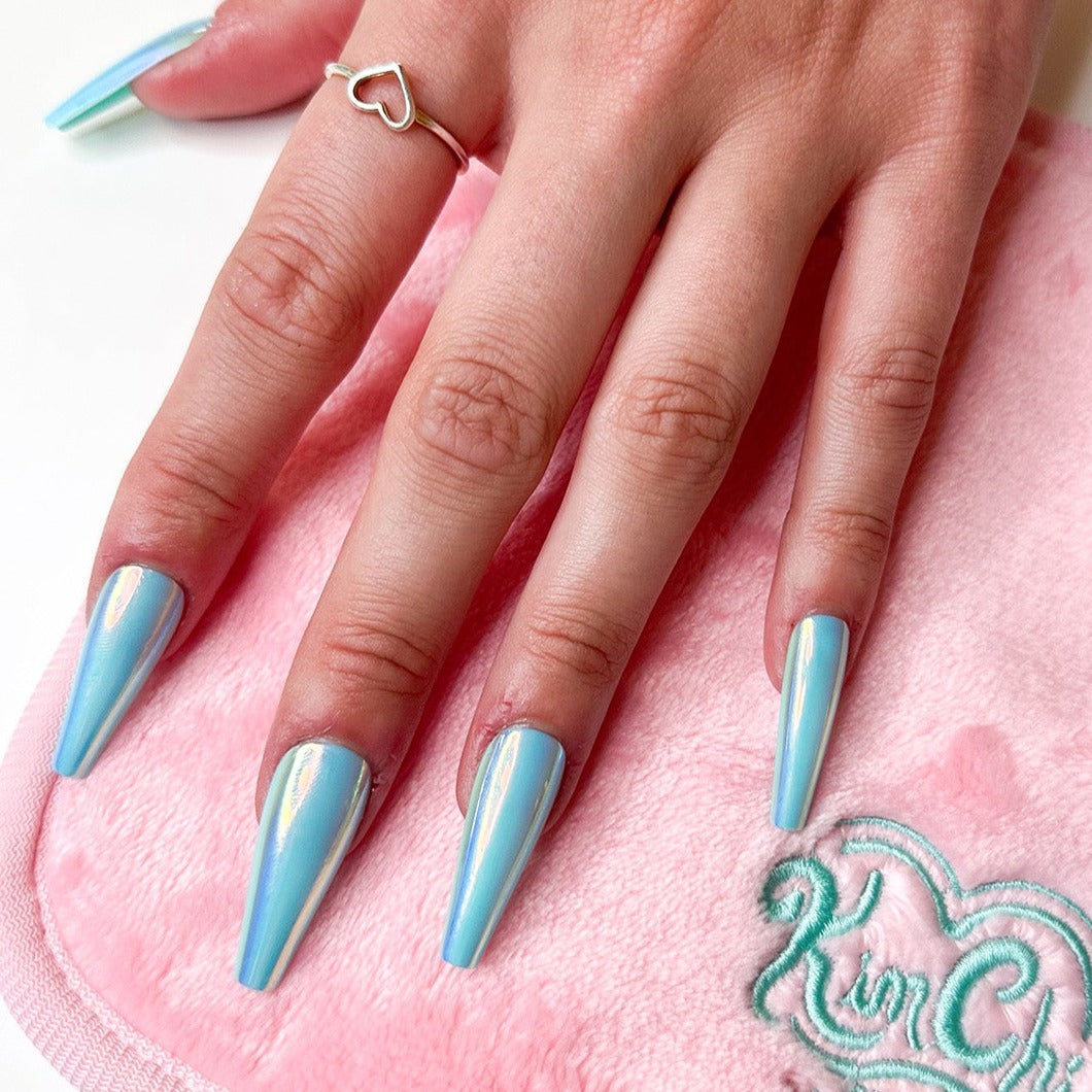 Hand with long, pointed light blue nails on a pink surface