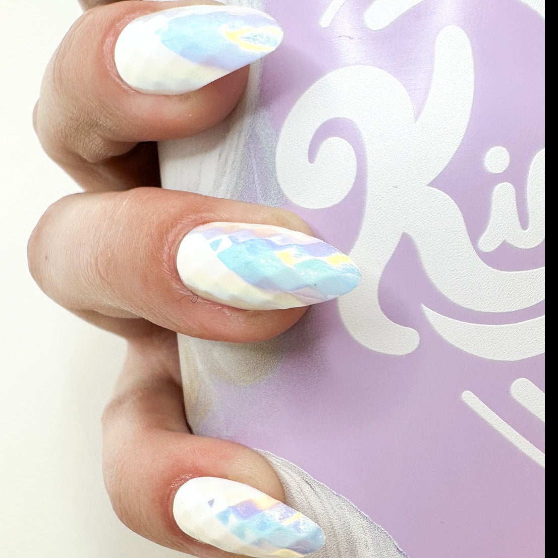 Hand with pastel geometric nail art holding a lavender can