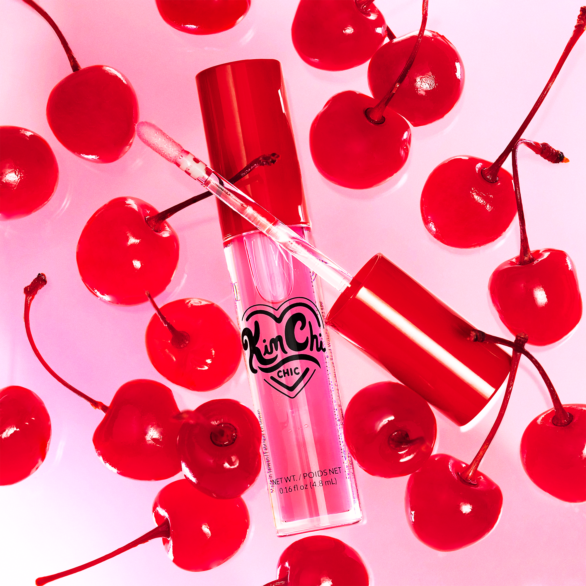 Kim Chi Chic cherry-flavored lip gloss in a red tube with cherries on a pink background.