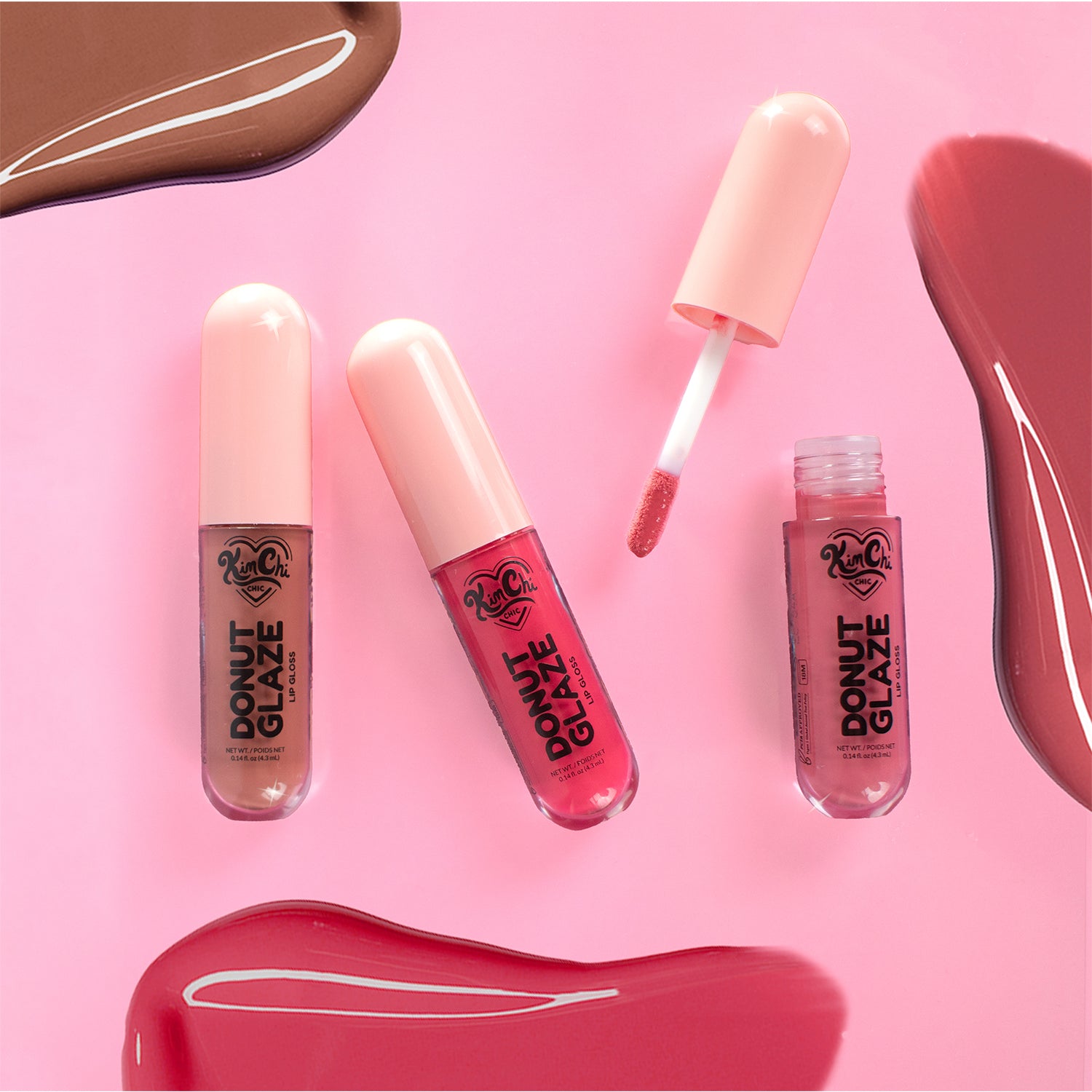 Three lip glosses from Donut Glaze arranged over a pink background with swatches of lip colors.
