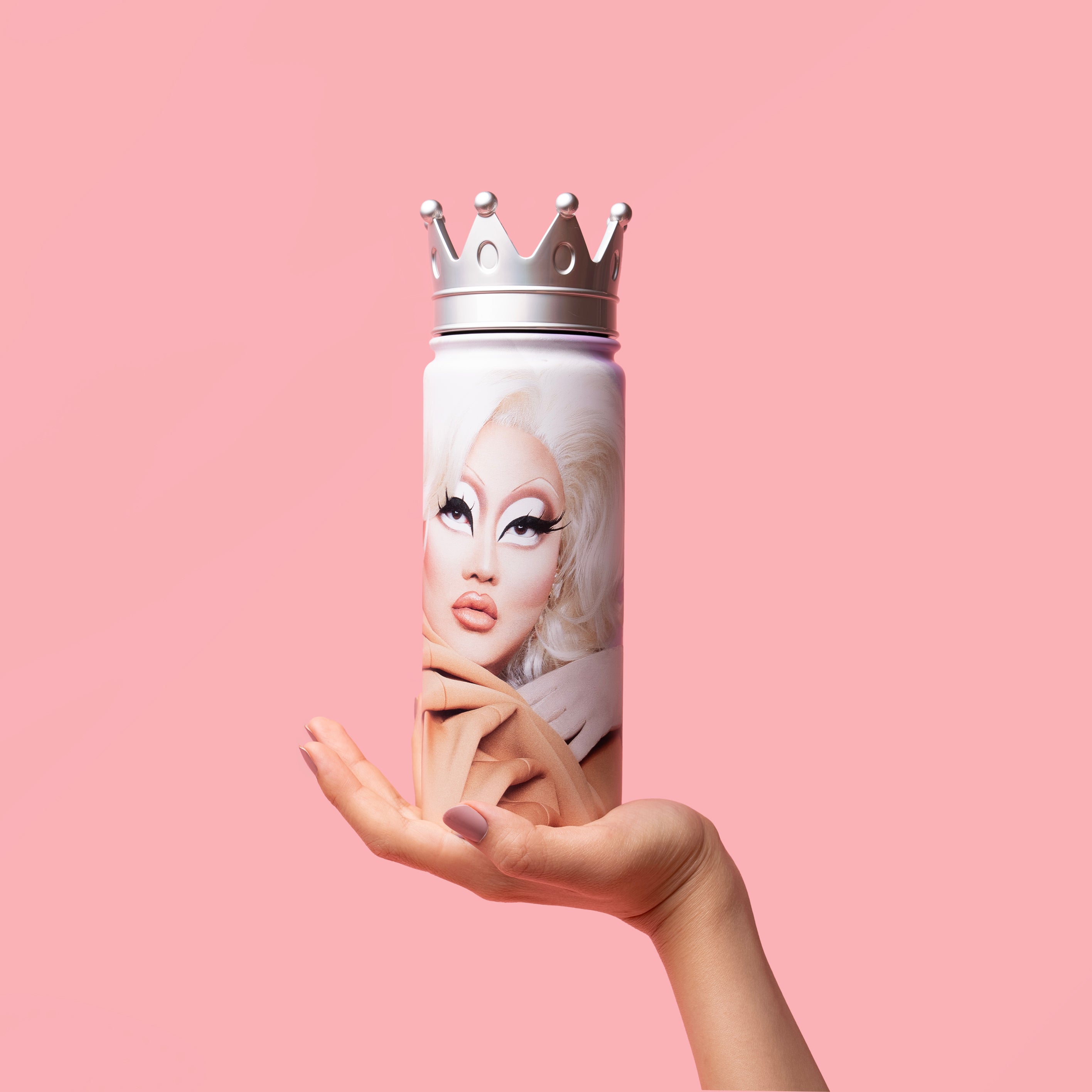 Hand holding a crowned bottle with a drag queen design on a pink background