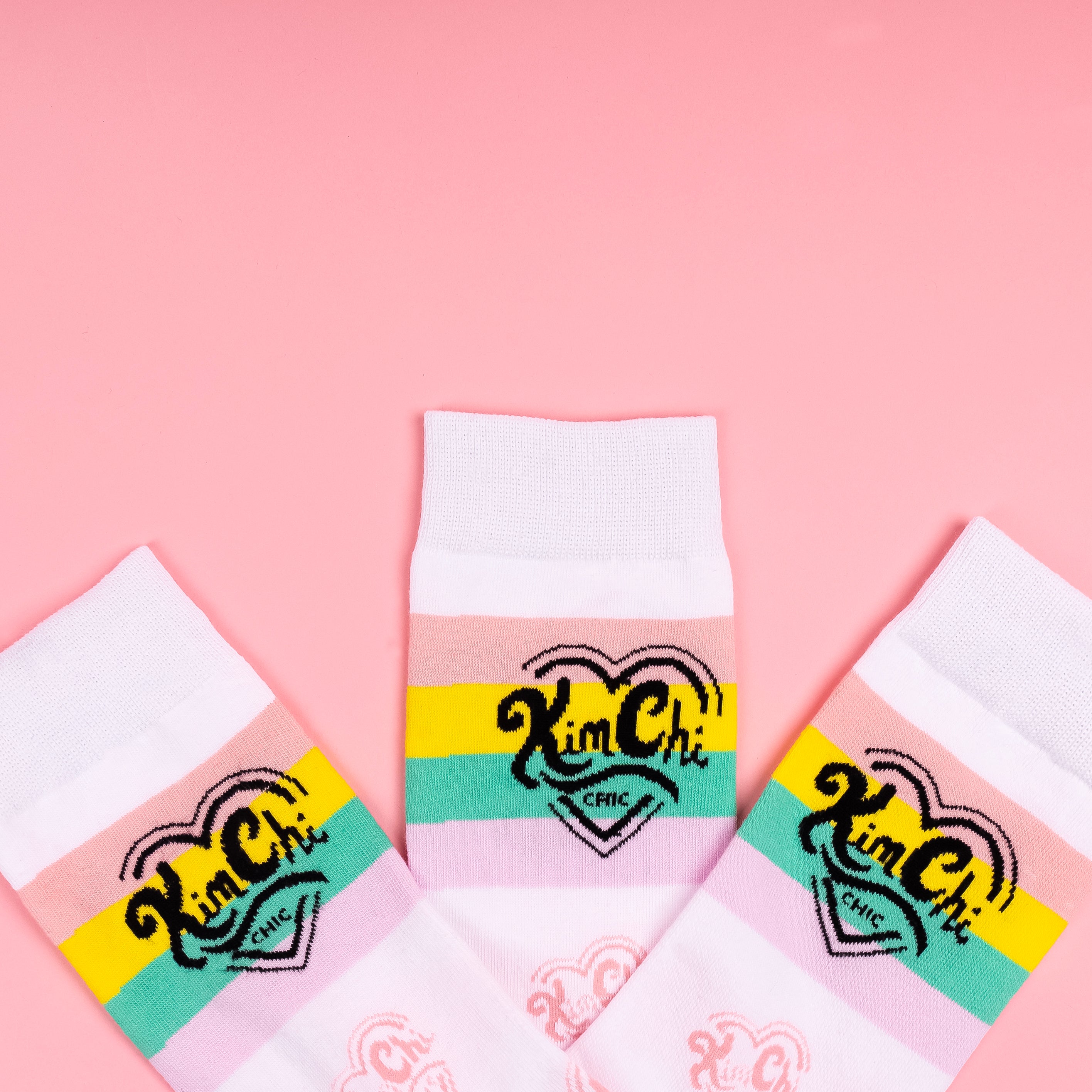 Three pairs of colorful socks with 'Kim Chi' logo on pink background.