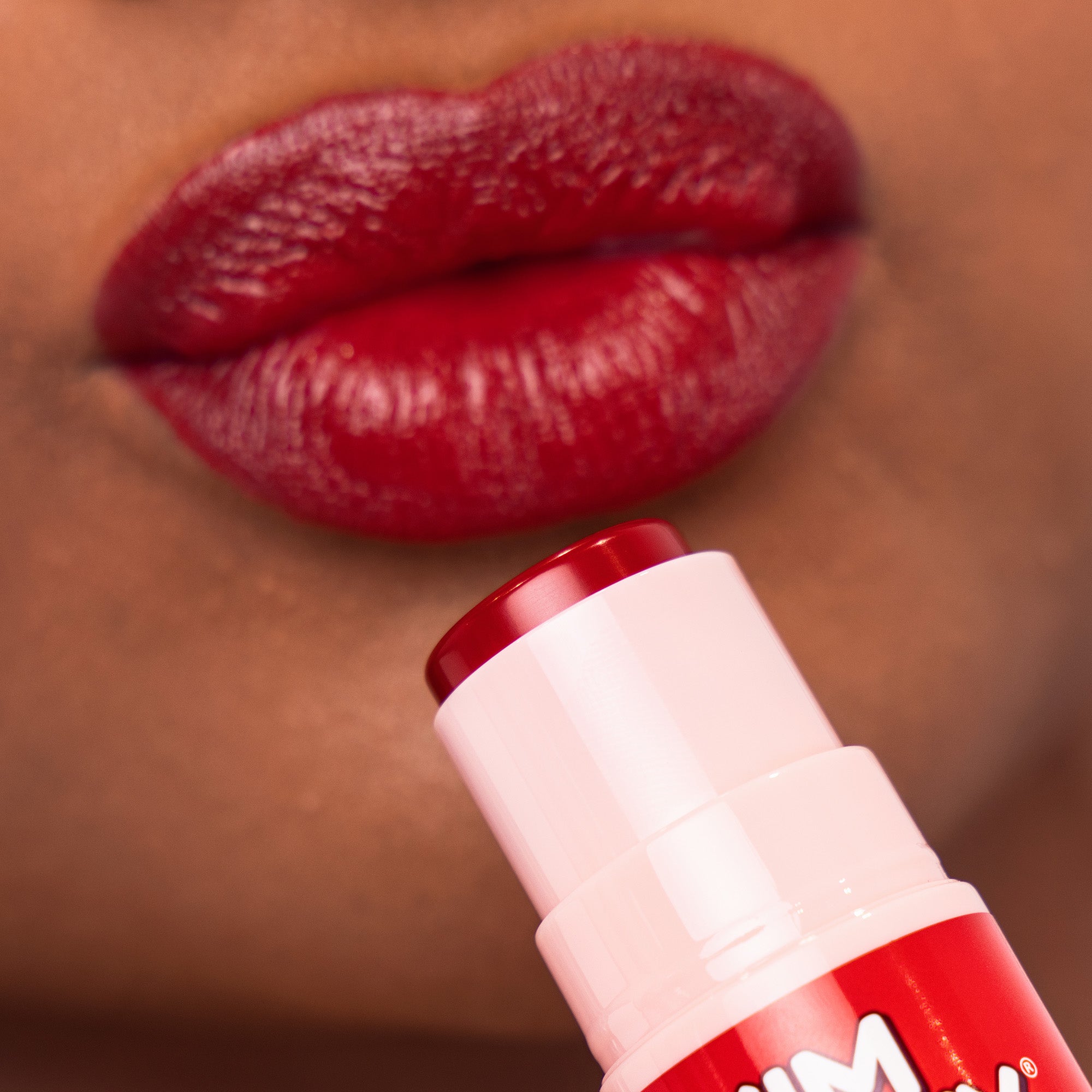 Close-up of red lips with a lip balm stick in the foreground
