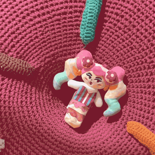 Colorful handmade doll with pink hair and unique design, resting on a vibrant crochet background.