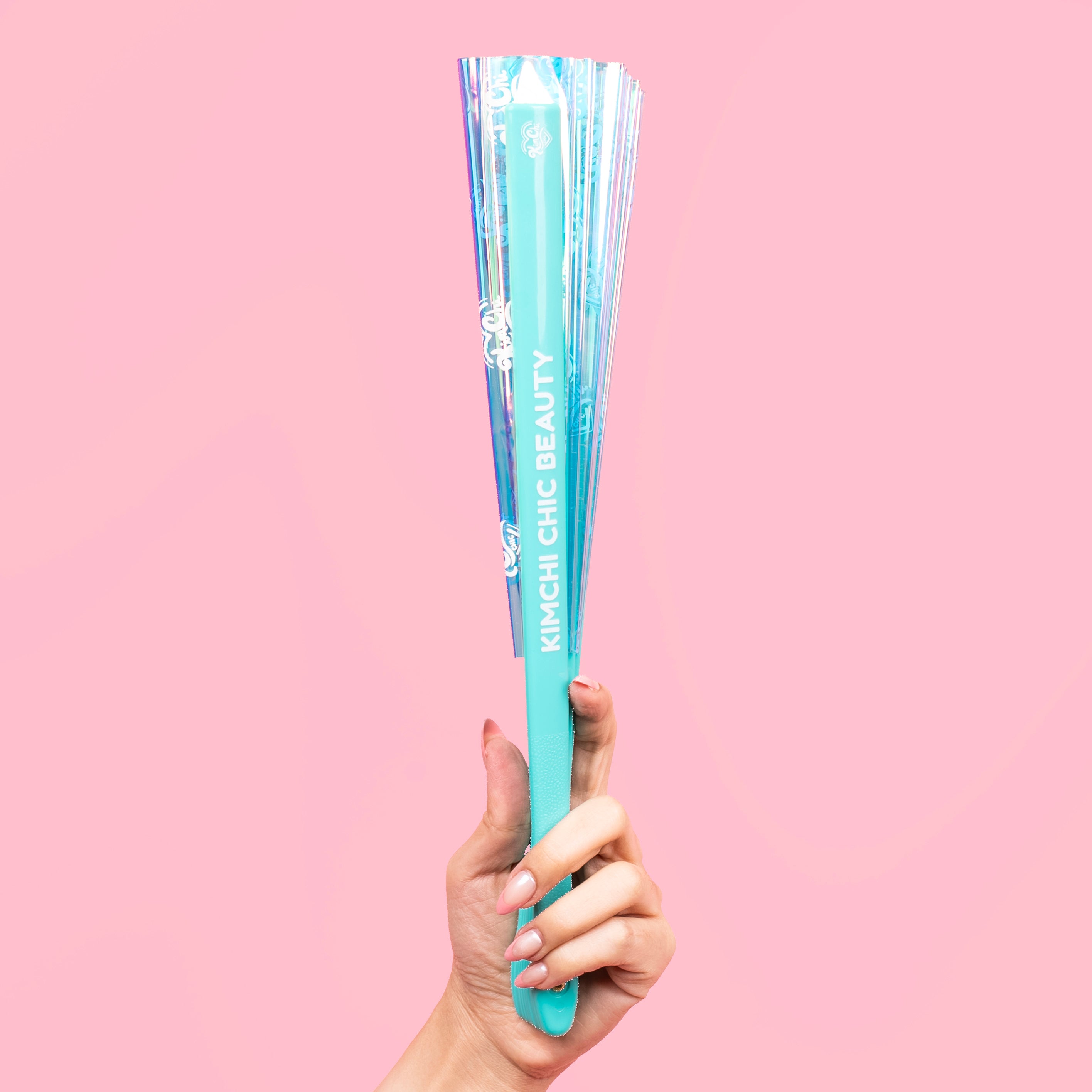 Hand holding a Korean beauty fan against a pink background.