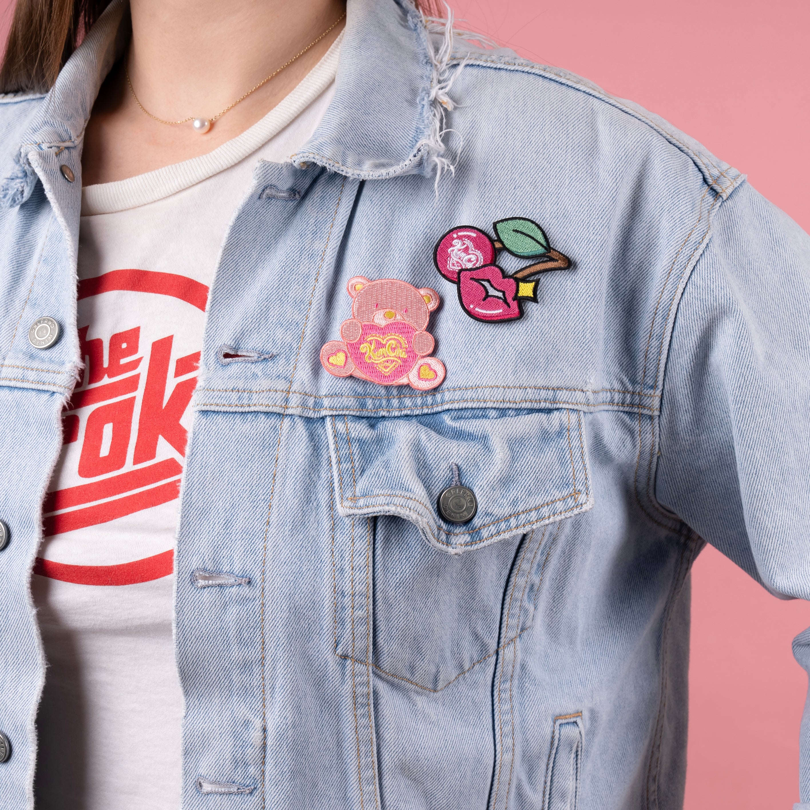 Person wearing a denim jacket with colorful patches and a graphic T-shirt underneath.