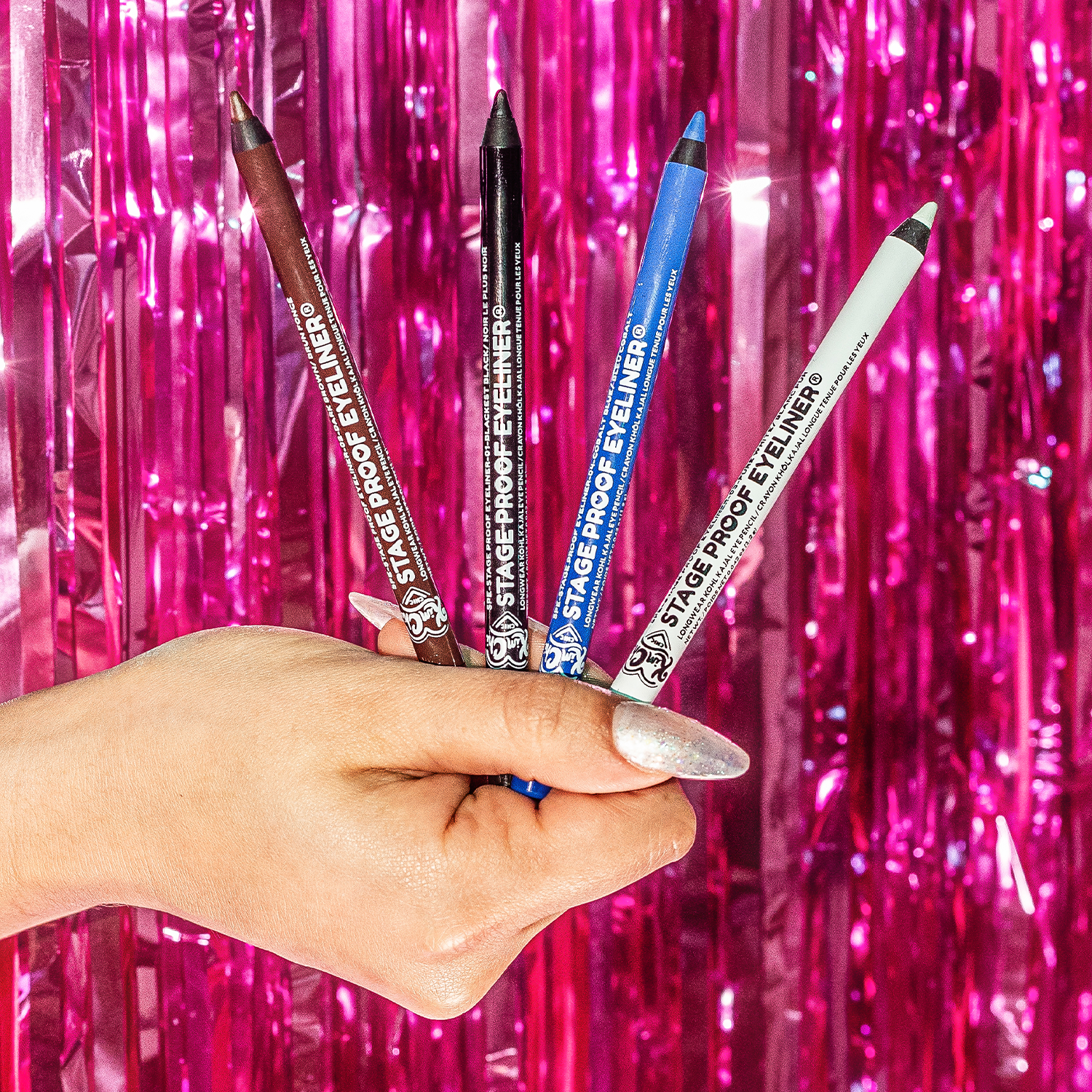 A hand holding four colorful eyeliners against a shiny pink background.