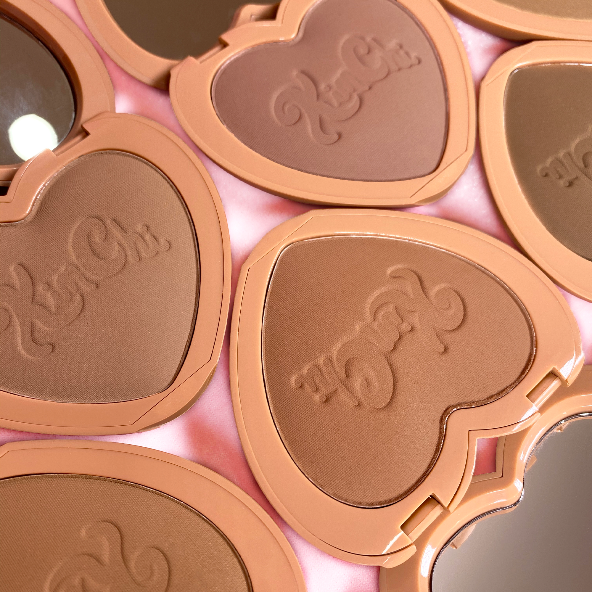 Heart-shaped bronzer compacts by Kim Chi, featuring rich tan shades and mirrored lids for easy application.