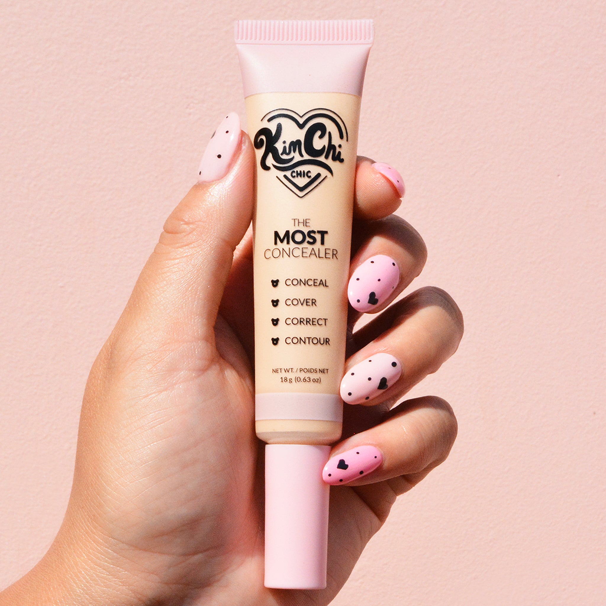 Hand holding a tube of Kim Chi The Most Concealer against a pink background.