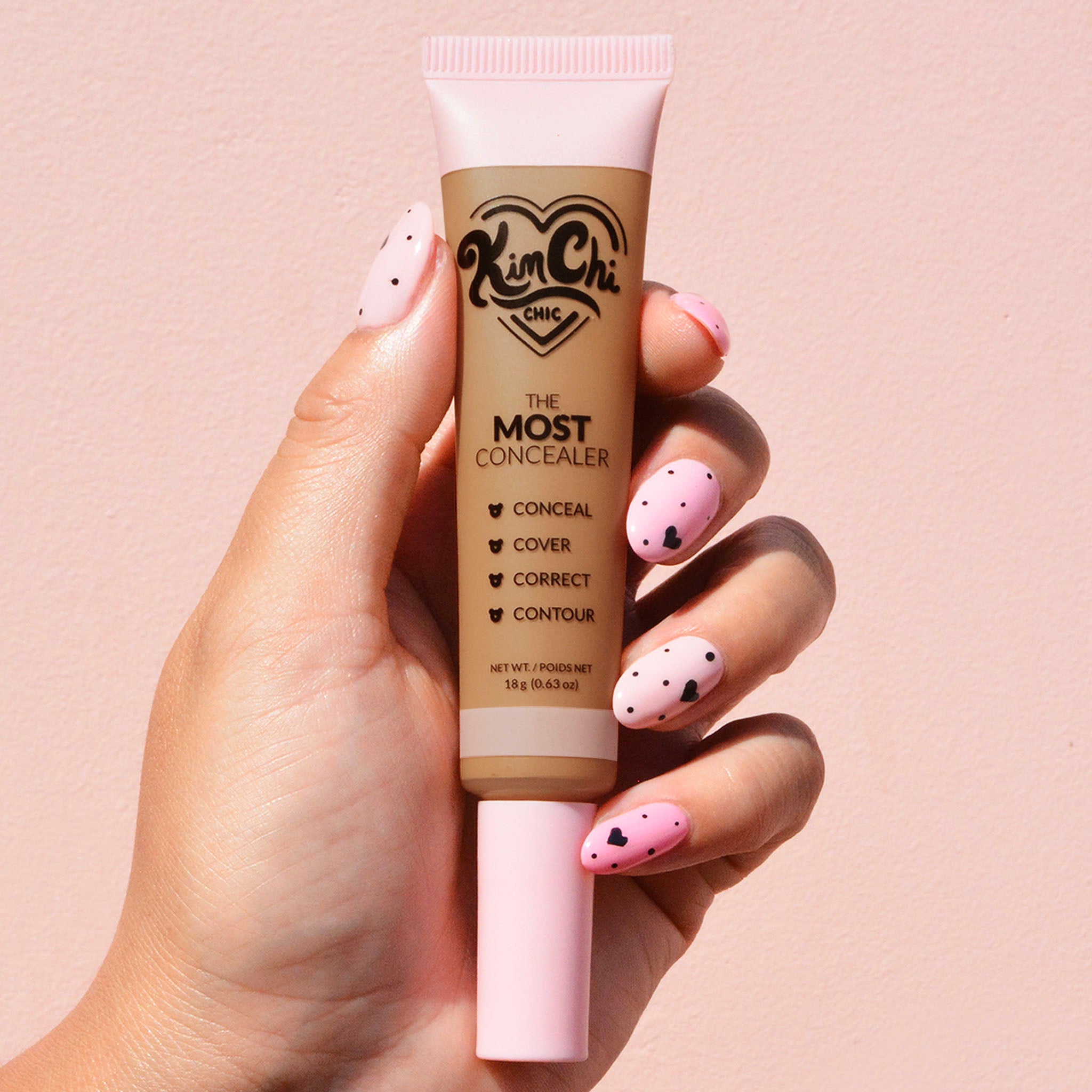 Hand holding Kim Chi Chic concealer tube against a pink background.