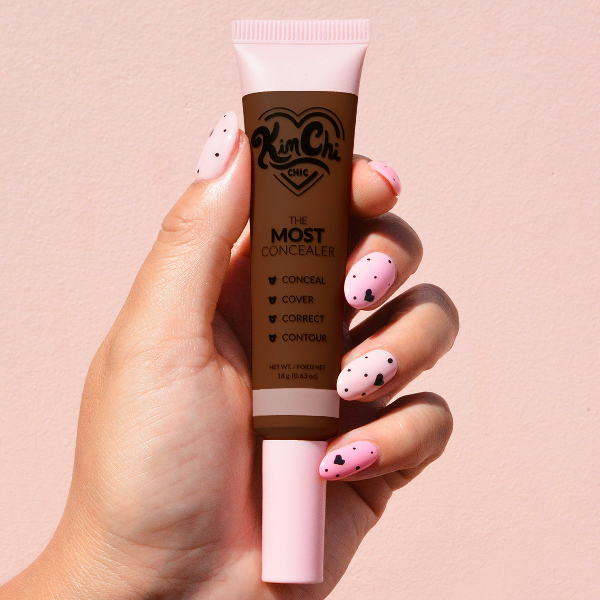 Hand holding KimChi Chic concealer tube against a pink background.