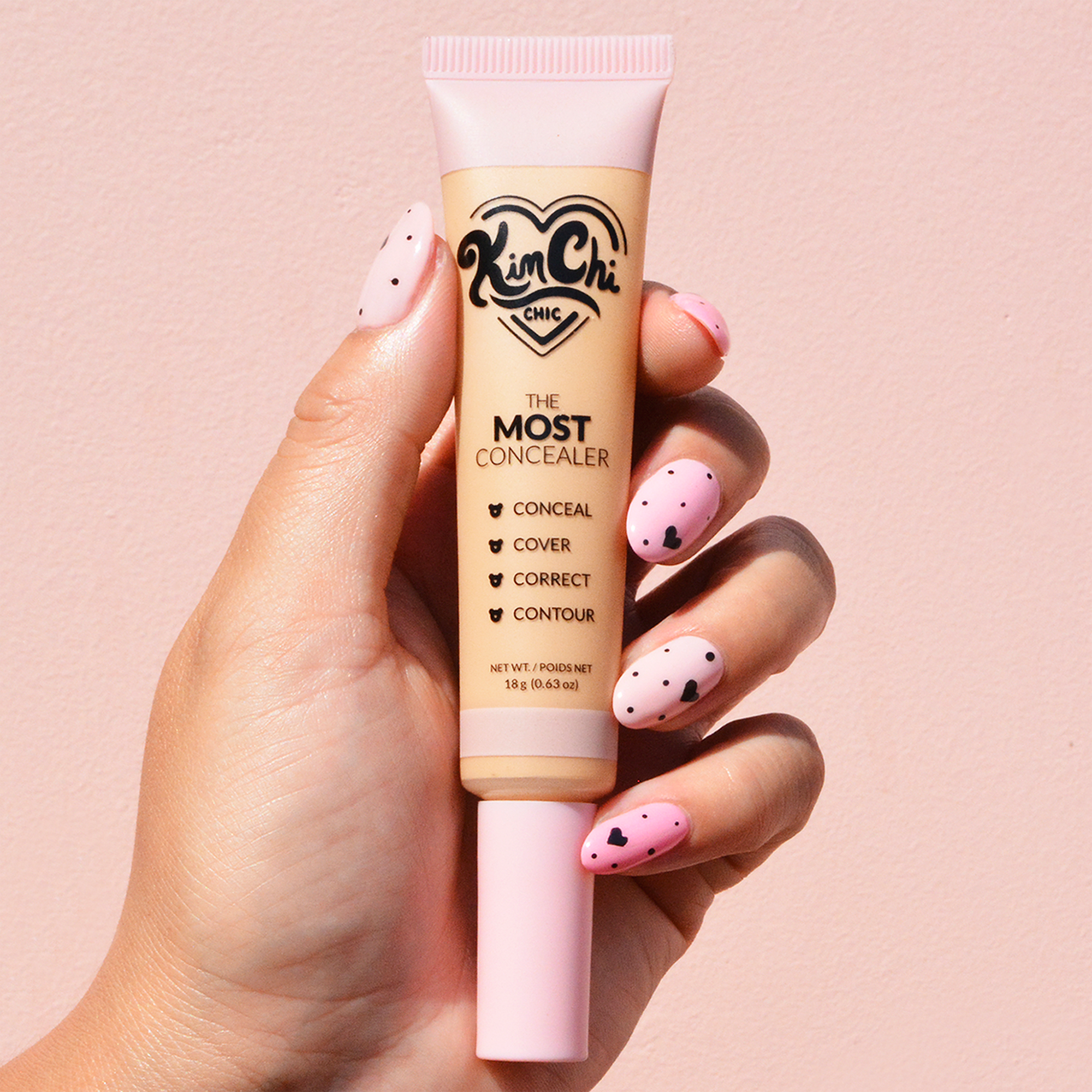 Hand holding a tube of Kim Chi Chic concealer against a pink background