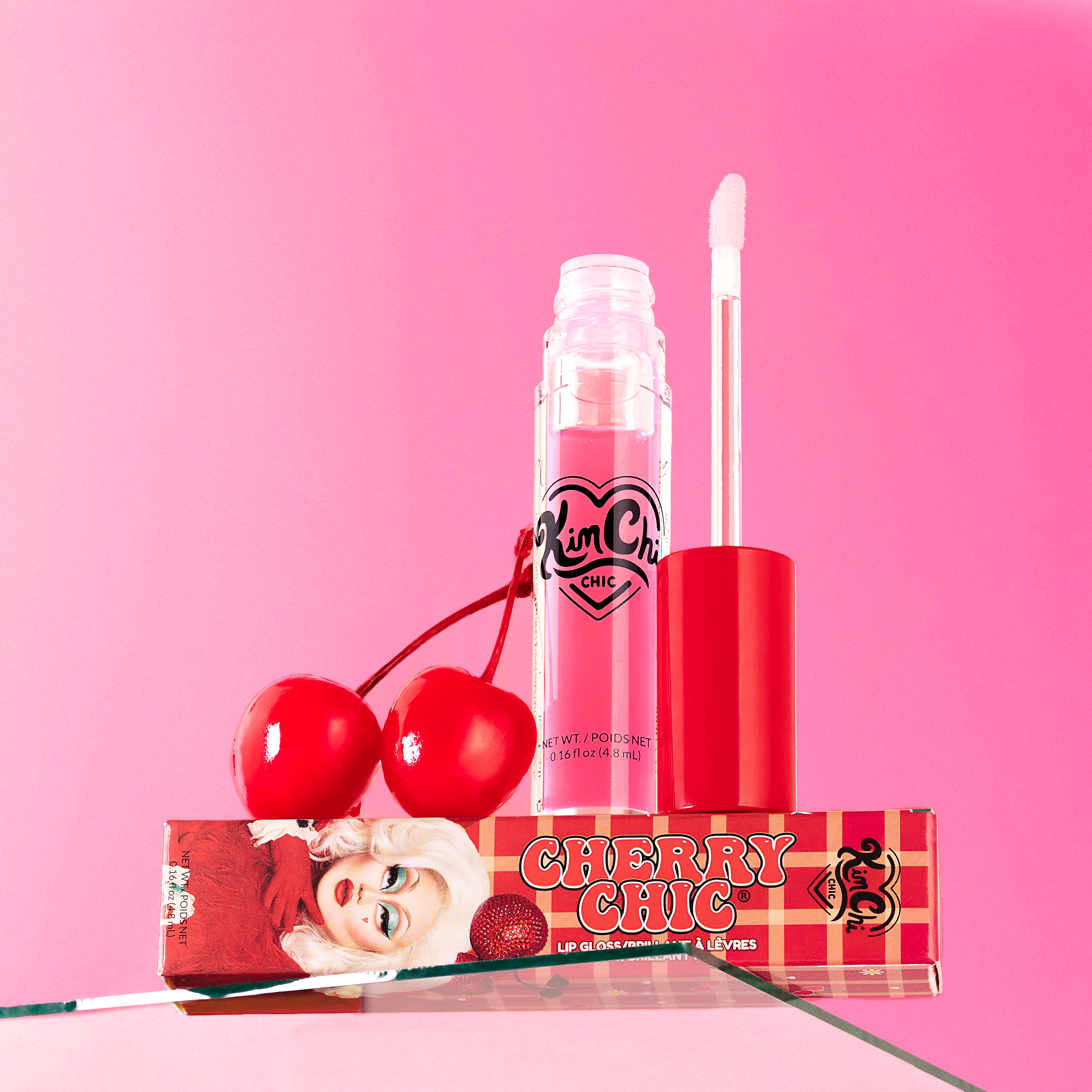 Cherry-themed lip gloss with packaging and cherries against a pink background.