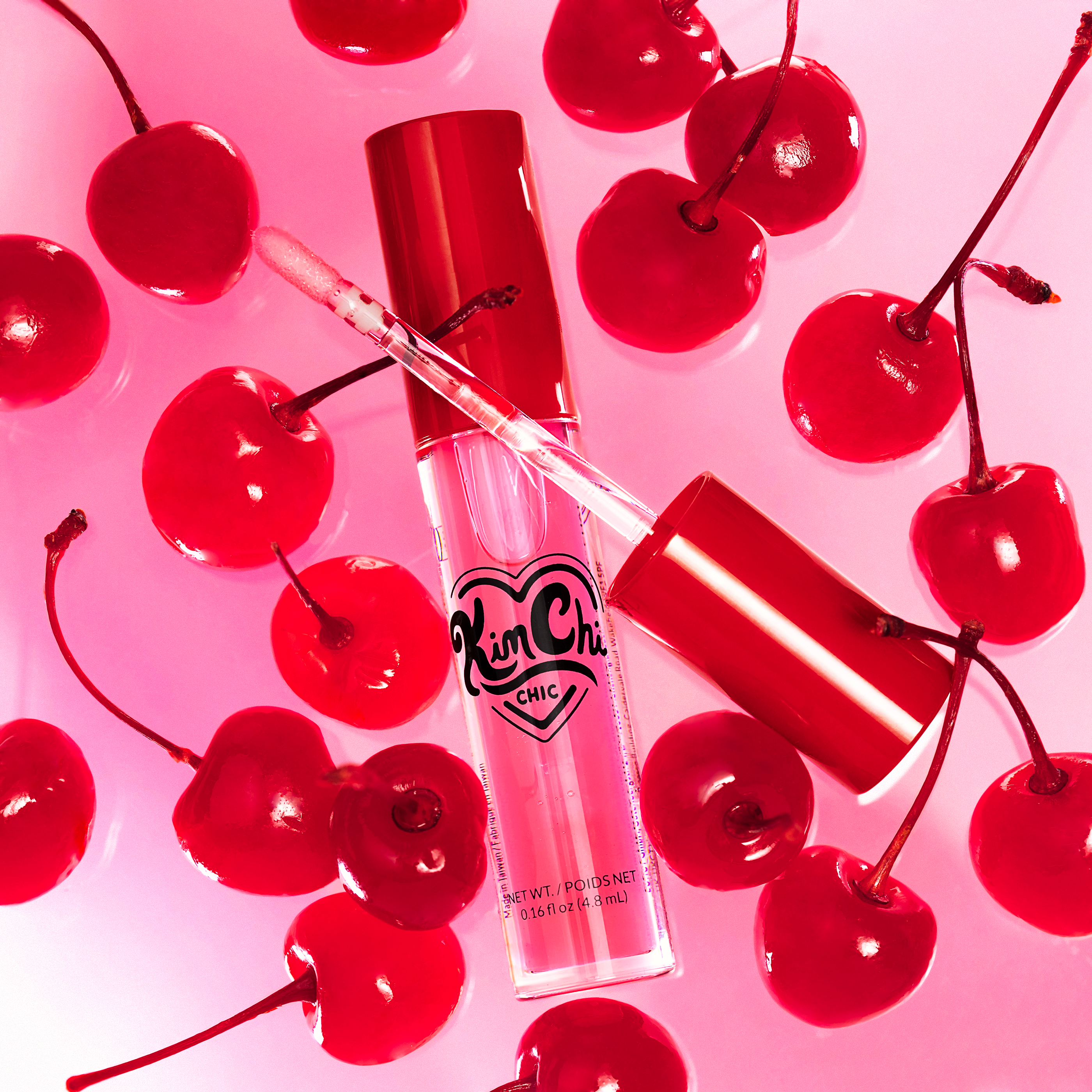 Lip gloss bottle surrounded by red cherries on a pink background