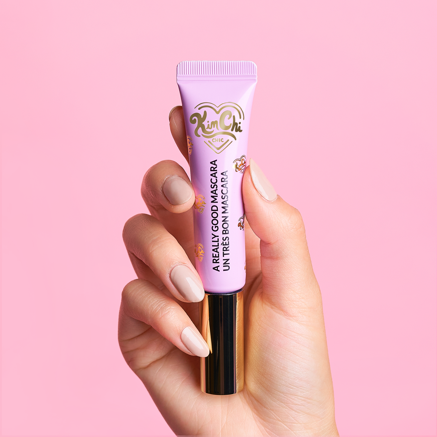 Hand holding a tube of mascara against a pink background