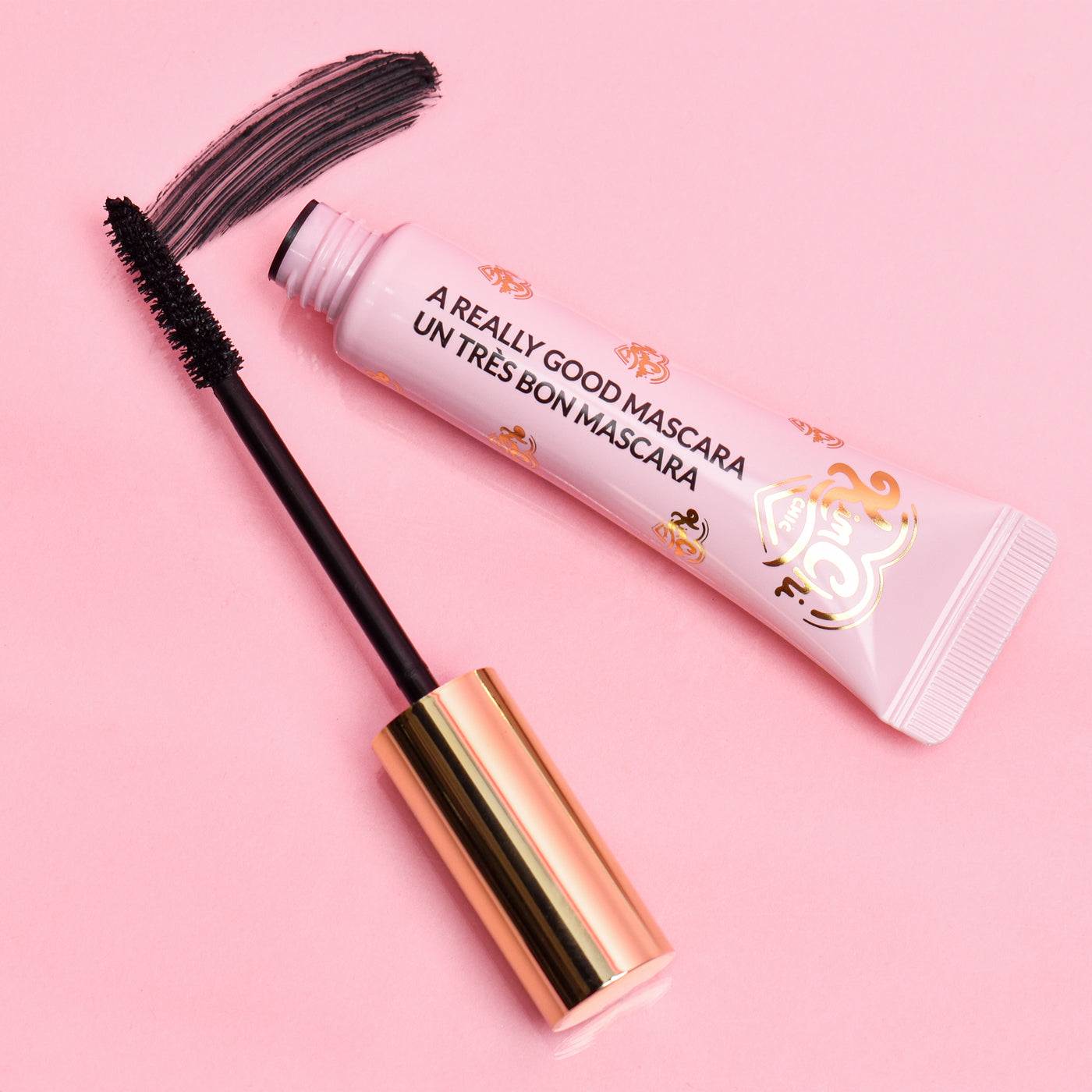 Mascara tube and applicator on a pink background