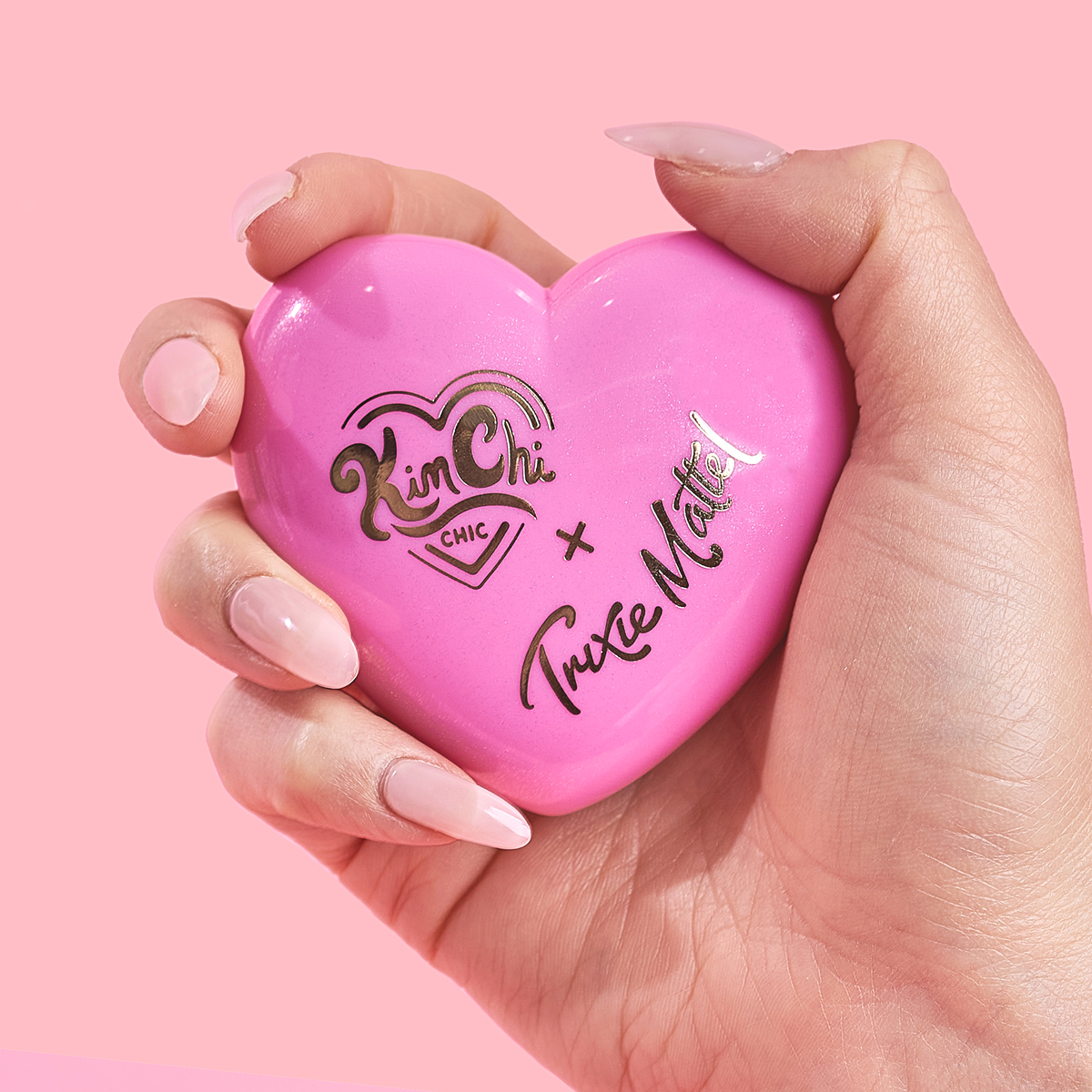 Hand holding a pink heart-shaped makeup compact.