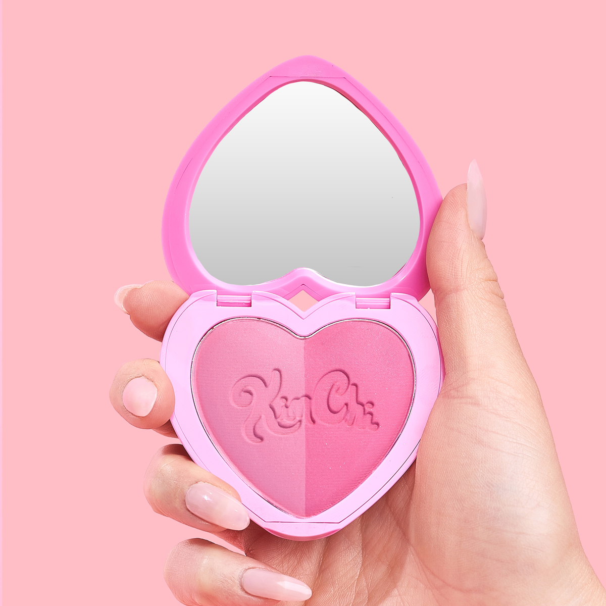 Heart-shaped pink makeup compact with mirror held in hand