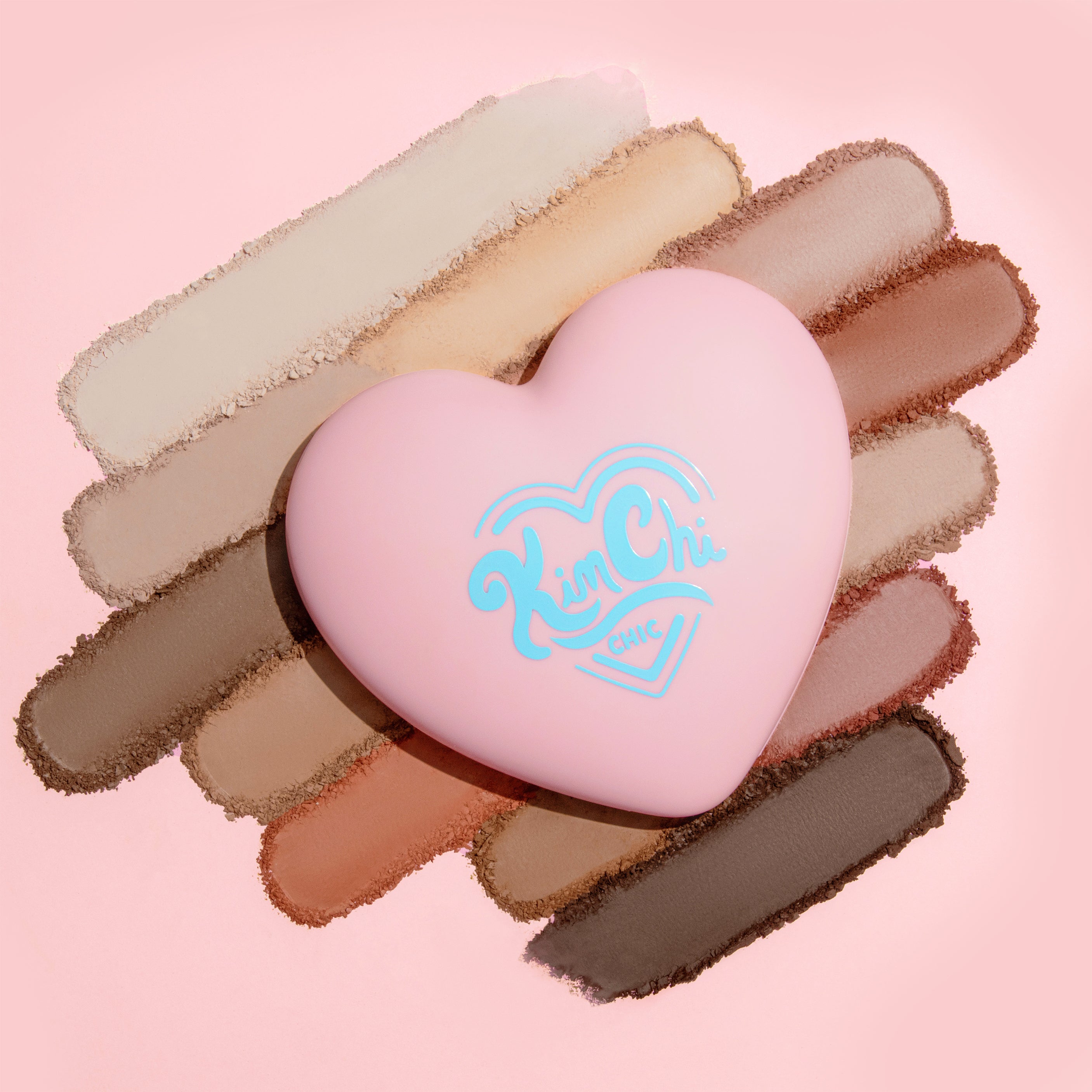 Heart-shaped pink makeup palette with various shades on a pink background.