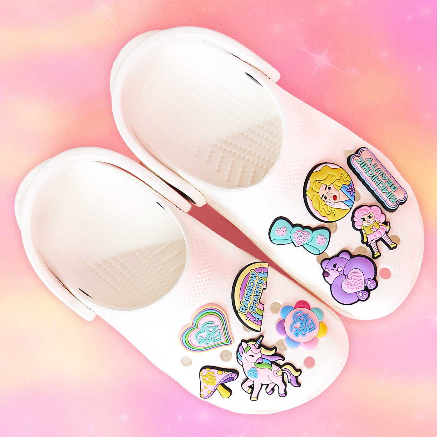 White children's clogs with colorful cartoon charms on a pink background.