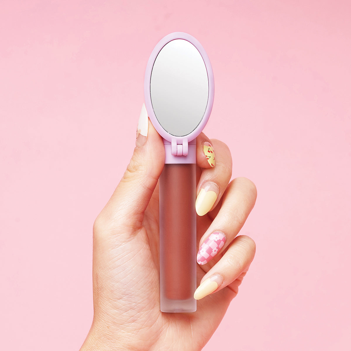 Hand holding a lip gloss with a small mirror attached, against a pink background.