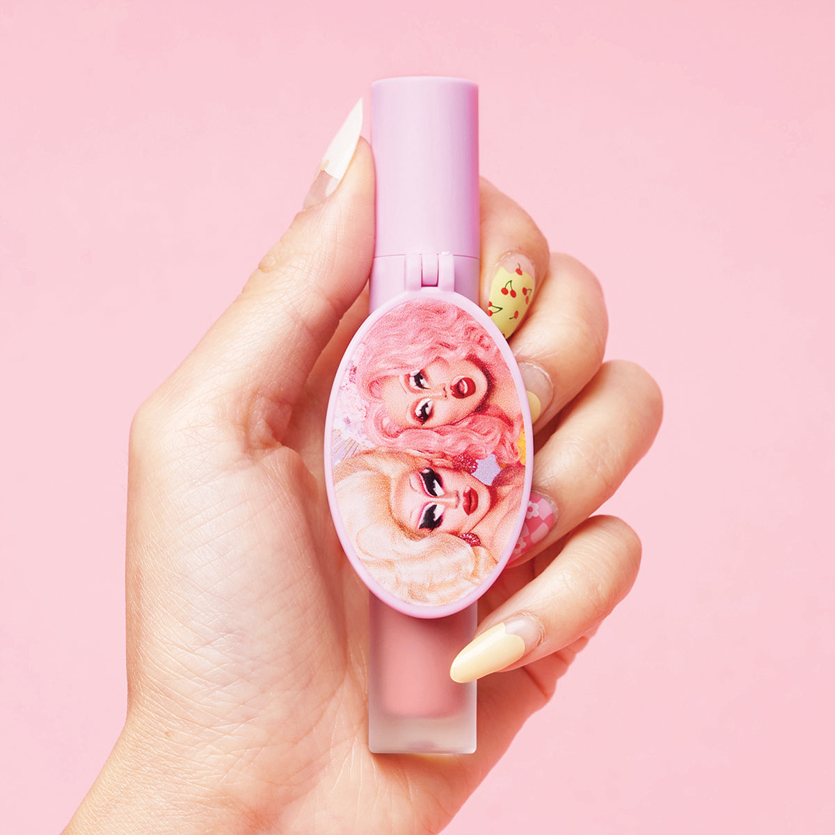 Close-up of a hand holding a pink lipstick tube with two cartoon characters on it against a pink background.