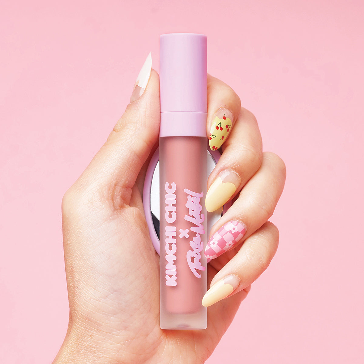 Hand holding a pink lipstick tube with decorative nails against a pink background.