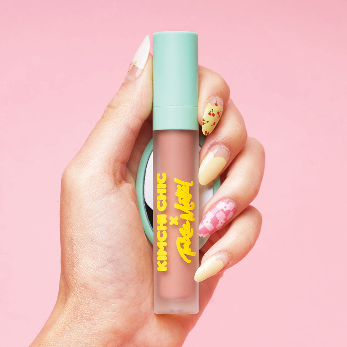 Hand holding a Kimchi Chic lip product with decorative nails against a pink background.