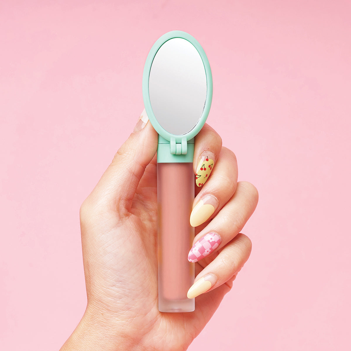 Hand holding lip gloss with a mirror attached, against a pink background.