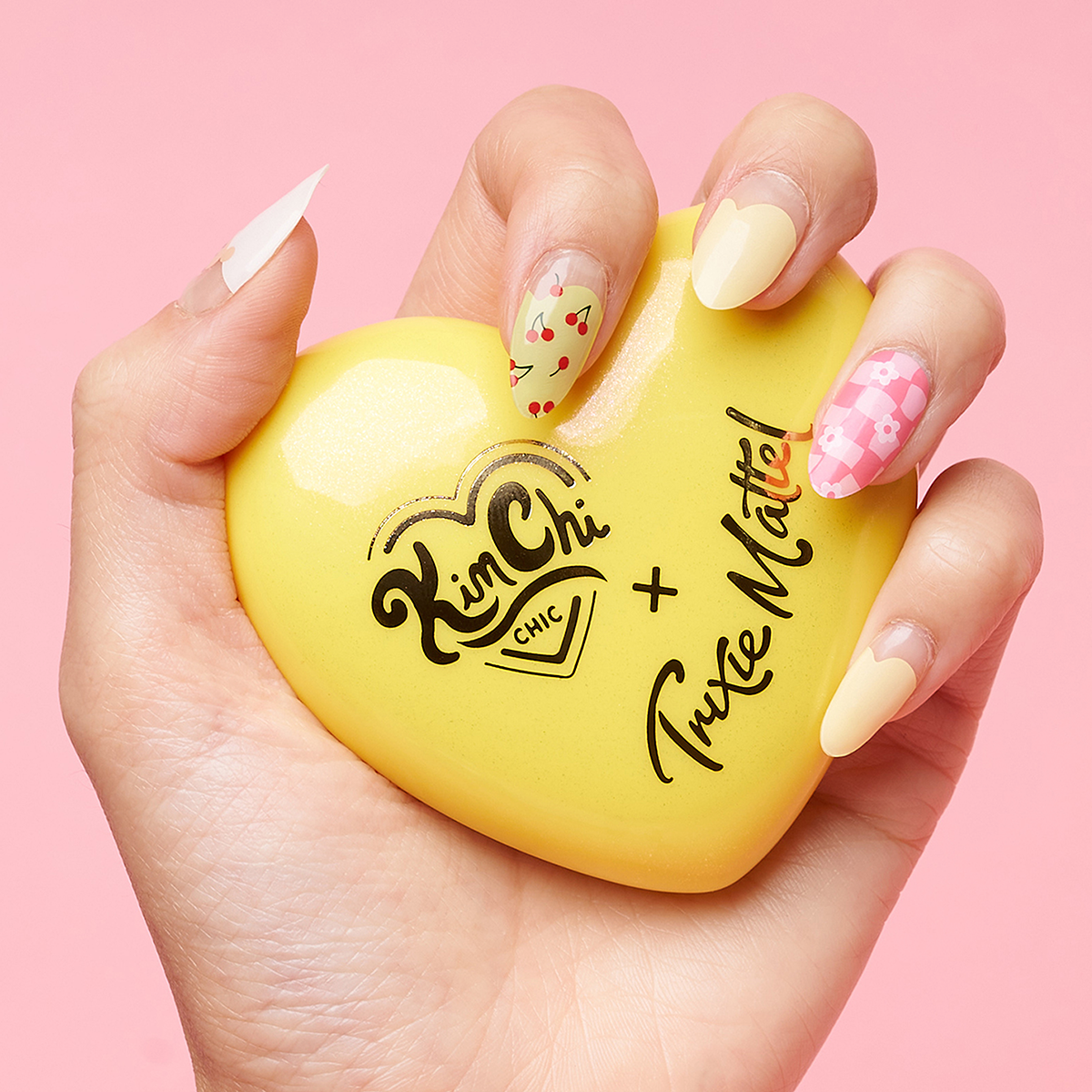 Hand holding a yellow heart-shaped compact with 'Kim Chi Chic x Trixie Mattel' text.